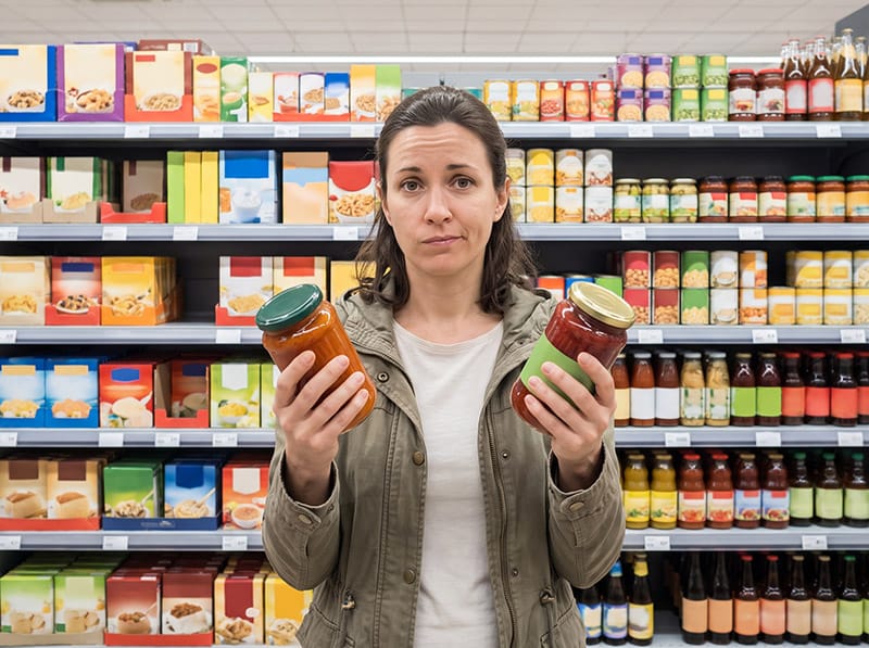 Shopper insights ilustrate printr-o cumpărătoare care compară două produse similare în fața raftului din supermarket